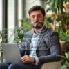 На фоне уютного интерьера, состоящего из мягкого освещения и стильной мебели, мужчина подчеркнуто выделяется своим стилем и концентрацией на работе. Ноутбук, открытый перед ним, символизирует связь с миром цифровых технологий и возможность путеводства в бесконечном пространстве информации и возможностей. Он является образцом профессионального подхода и уравновешенности между работой и жизнью